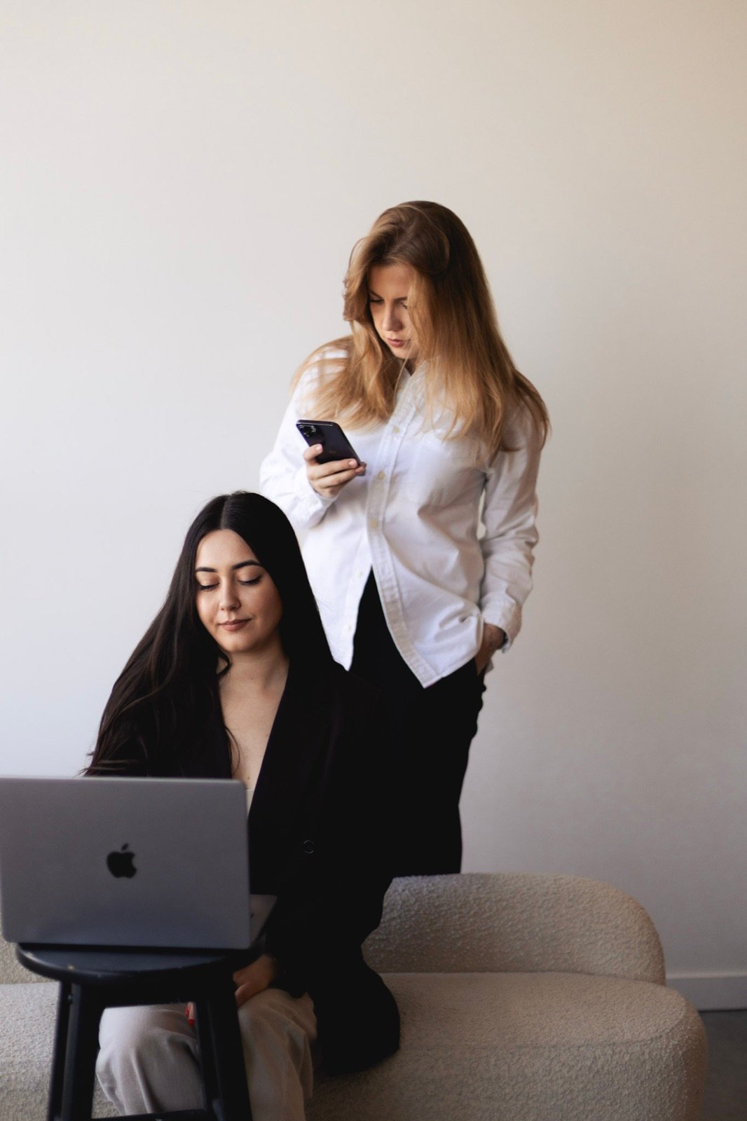 A Syntri Labs team member checking a phone while a colleague works at a laptop.